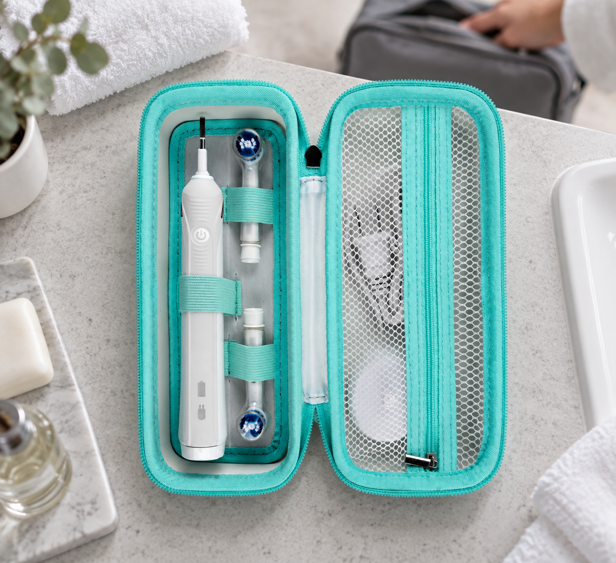 Open teal ALKOO electric toothbrush case with retaining bands and white mesh pocket on a hotel vanity