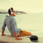 Man wearing headphones beside the closed black and red travel case at a waterfront