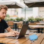 Light blue portable SSD case beside a laptop at an outdoor cafe