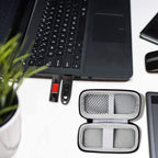 Black USB flash drive and SD card storage case open interior holding drives beside a laptop