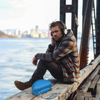 Man resting at a waterfront beside the open blue headphone case