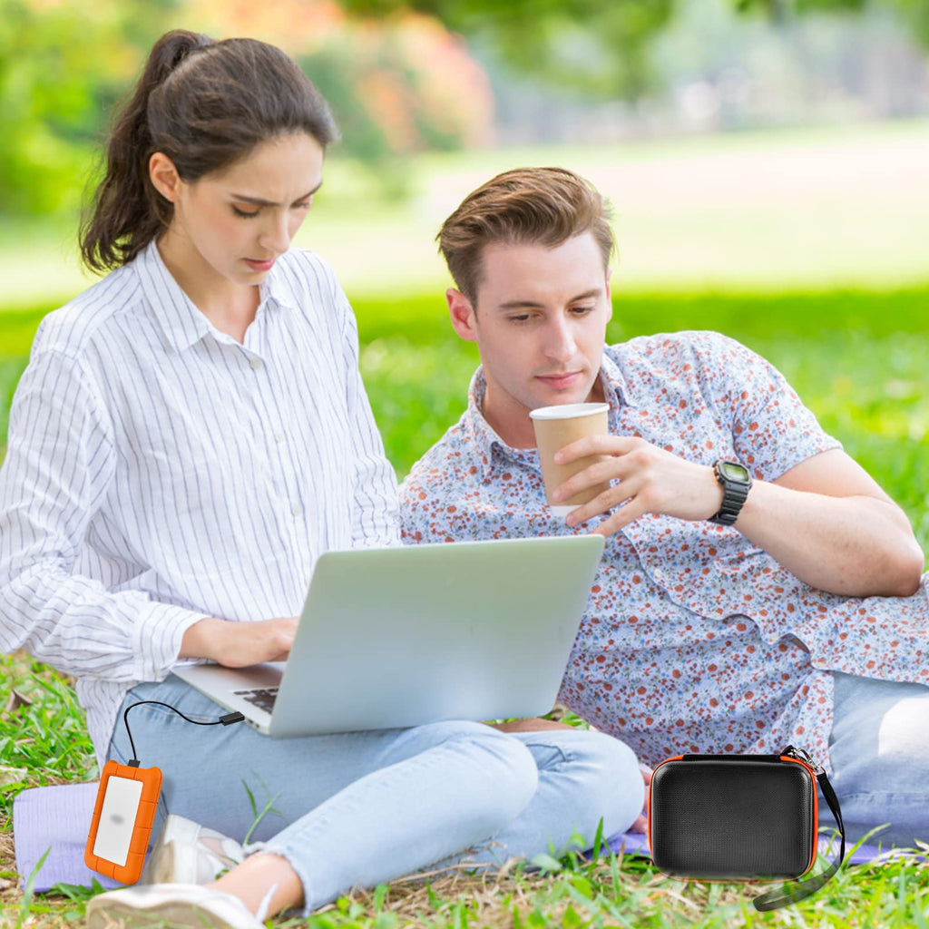 Black and orange hard drive case beside a portable drive during outdoor laptop use