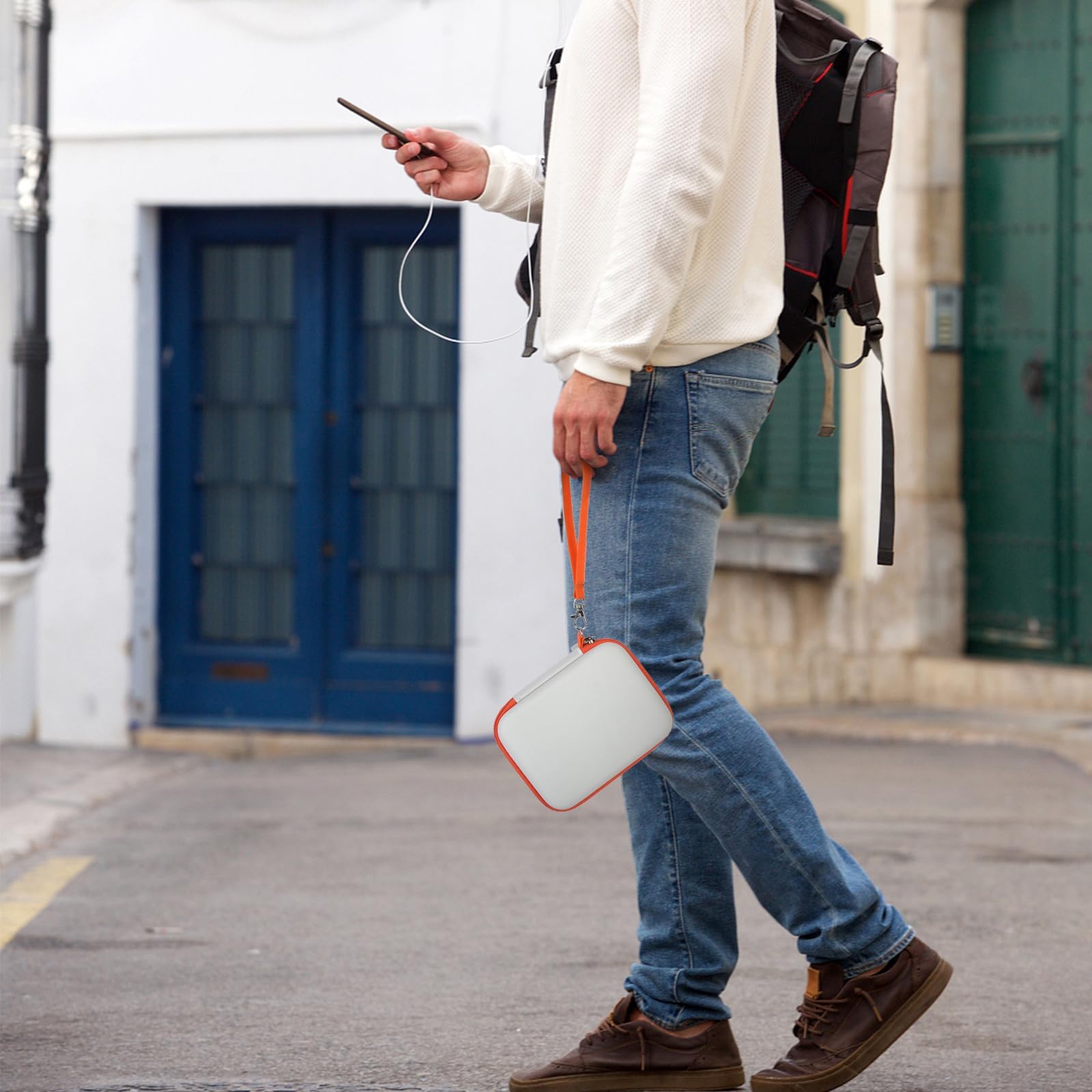 Person carrying the gray and orange portable hard drive case by its wrist strap