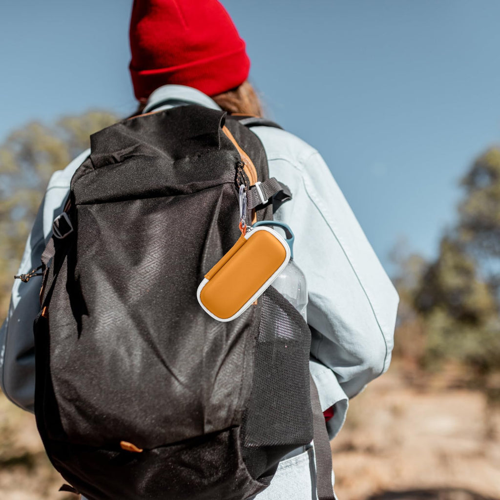 Orange KardiaMobile case clipped to a hiking backpack