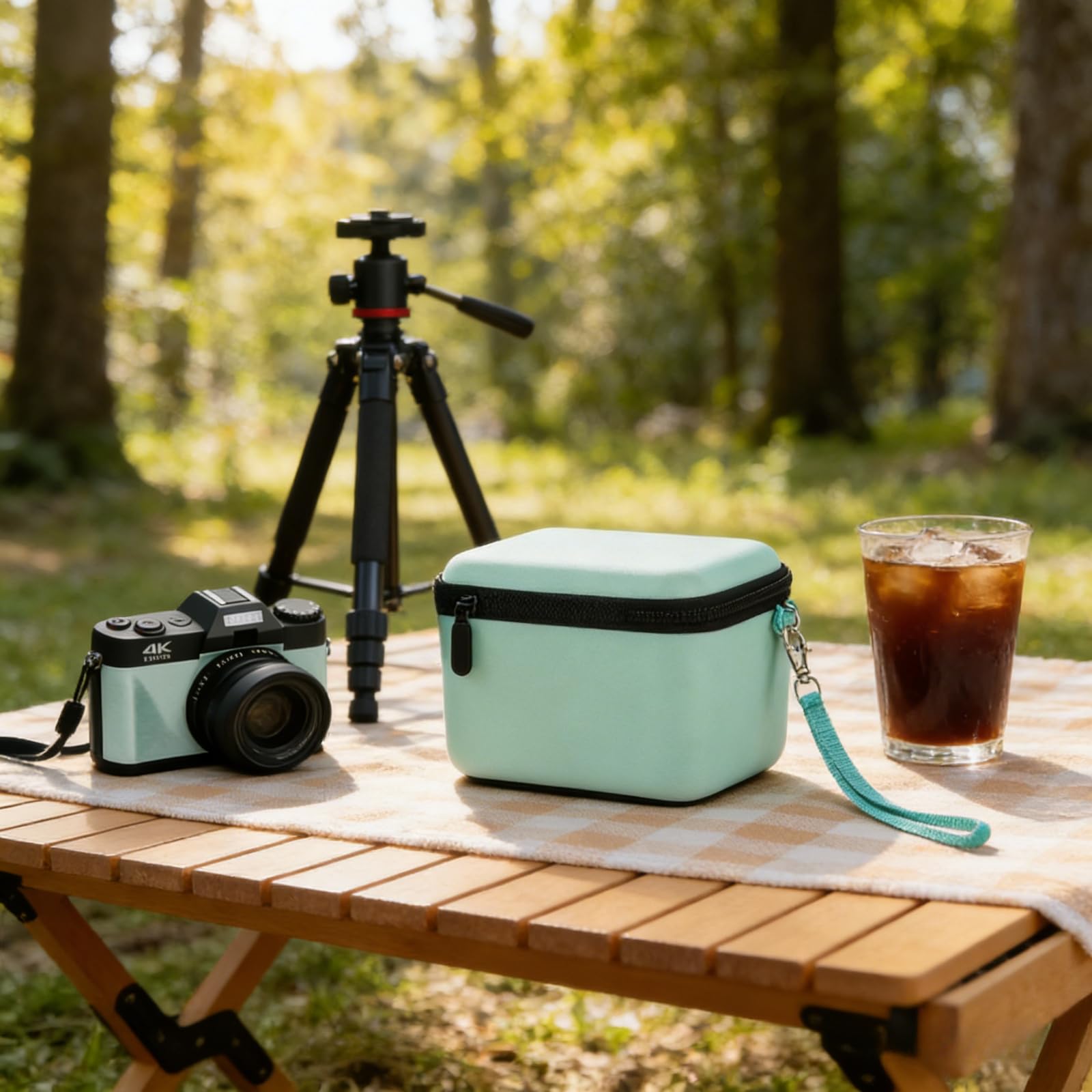 Mint green camera case beside a compact camera and tripod at an outdoor campsite